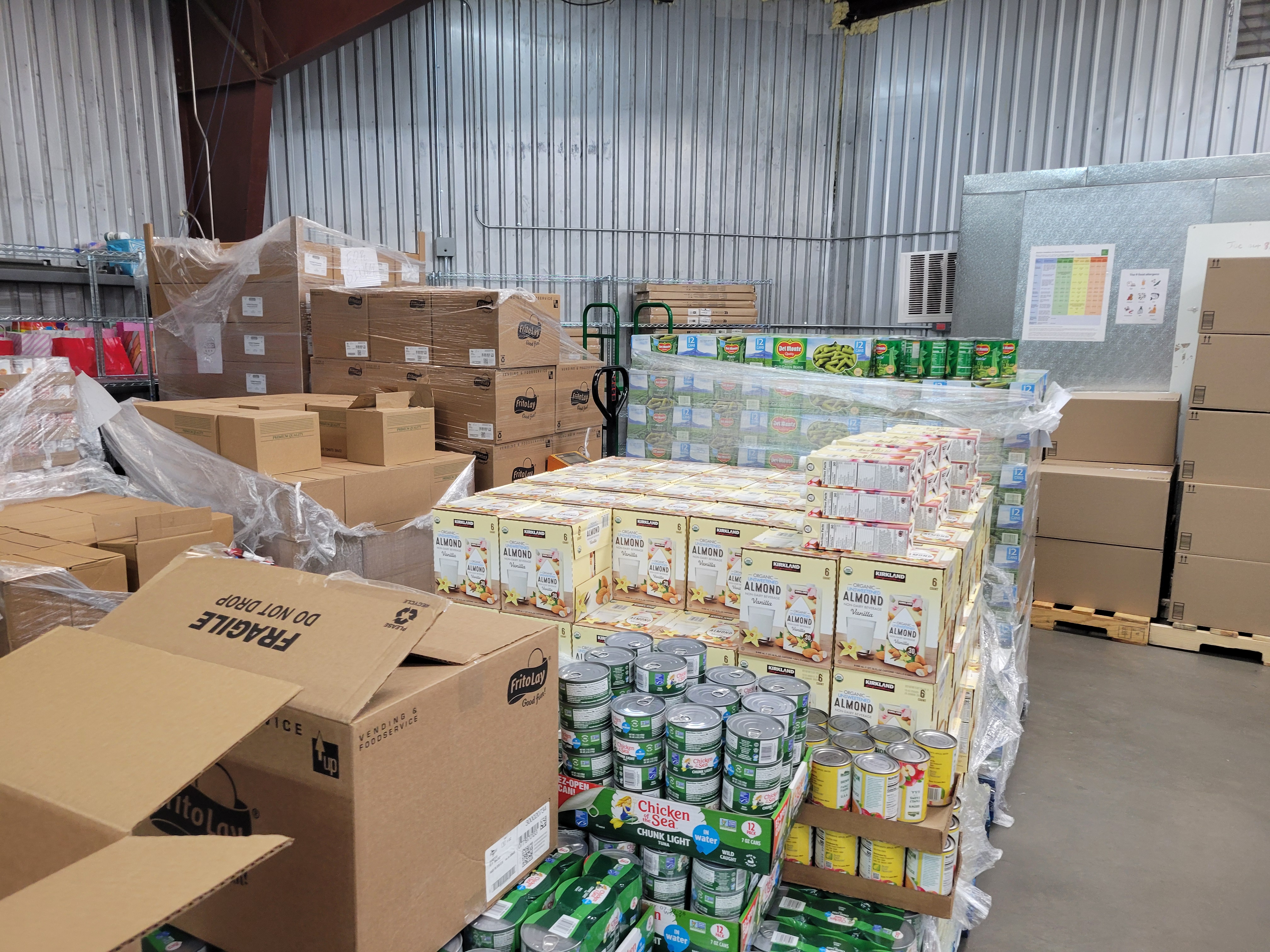 Pallet of canned tuna. box of almond milk, and canned green beans next to each other.